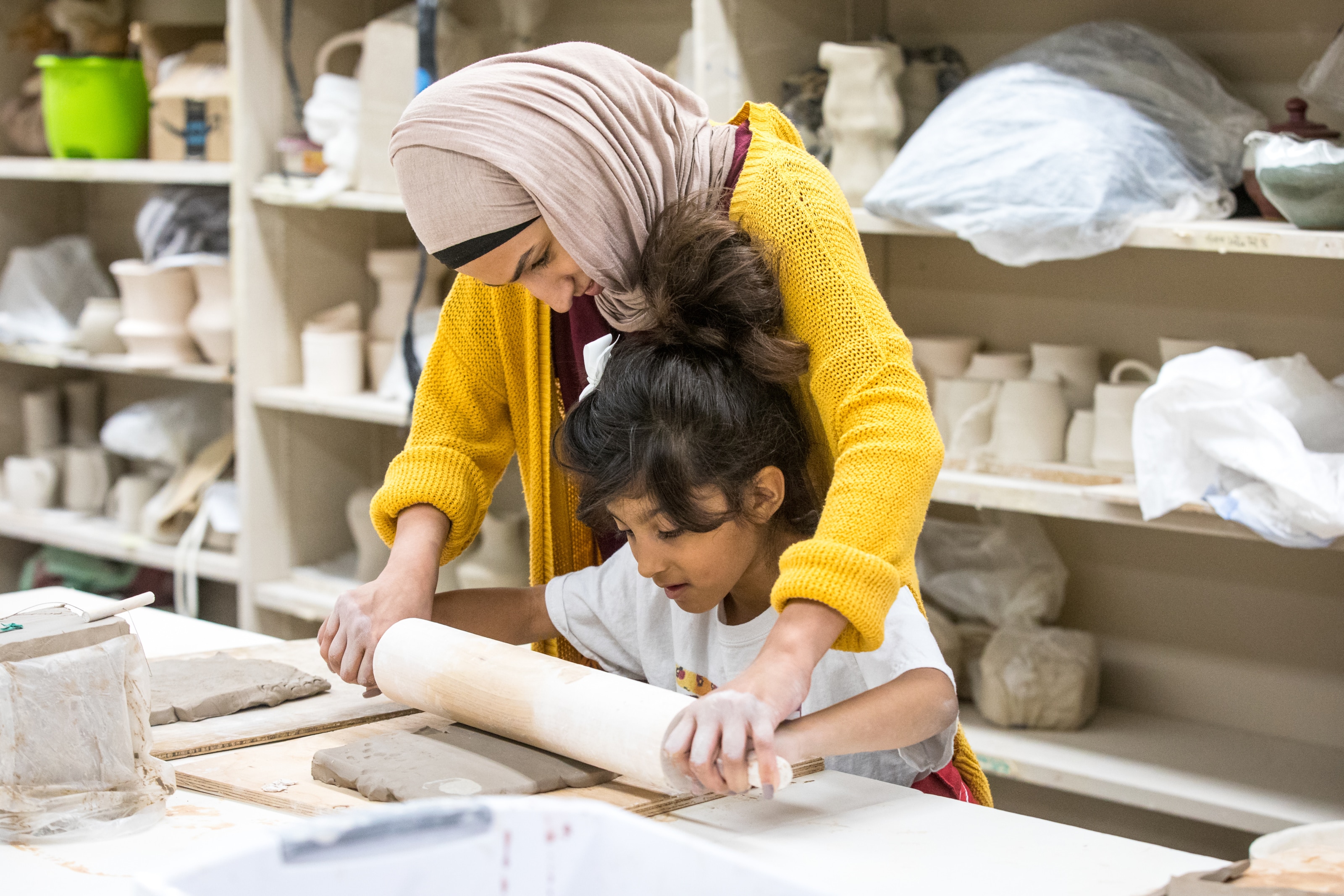 student helps her daughter roll a slab of clay